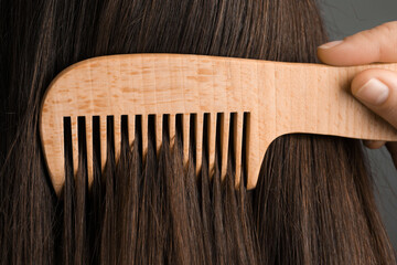 Obraz premium Woman brushing hair with wooden comb on grey background, closeup
