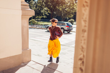 Young woman walking on city street wearing brown cashmere sweater and yellow skirt outfit with...