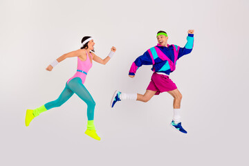 Energetic young couple in vibrant retro activewear joyfully leaping with excitement on a white background.