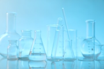 Blurred view of laboratory glassware on mirror surface against light blue background
