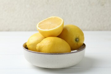 Fresh whole and cut lemons in bowl on white wooden table, closeup