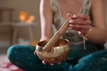 Woman with singing bowl and burning candles indoors, closeup