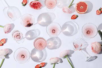 Flat lay composition with rose wine in glasses and flowers on white background