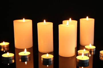 Many burning candles on mirror surface against black background, closeup
