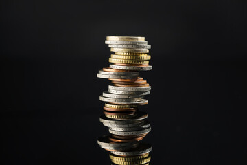 Many stacked coins on dark mirror surface, closeup