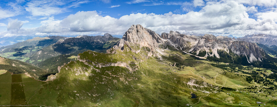 High resolution panoramic drone shot of the iconic Seceda plateau in the Dolomites, Italy. The view reveals the entire ridge, lush meadows, and surrounding valleys with remarkable detail