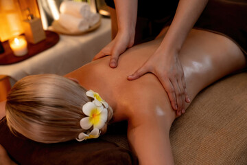 Closeup woman customer enjoying relaxing anti-stress spa massage and pampering with beauty skin recreation leisure in warm candle lighting ambient salon spa at luxury resort or hotel. Quiescent