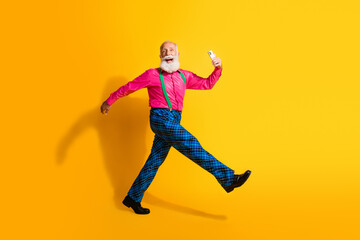 Full body photo of bearded gentleman excited walk hold device wear fashionable clothes suspenders isolated on vibrant yellow background