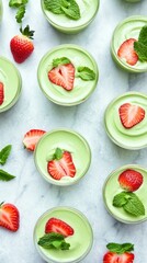 Fototapeta premium Sweet Delight: Overhead shot of refreshing green dessert cups elegantly garnished with fresh strawberries and mint leaves.