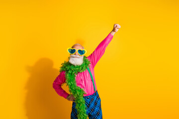 Photo of nice senior male raise fist superhero boa wear pink shirt plaid pants suspenders fancy outfit isolated on yellow color background
