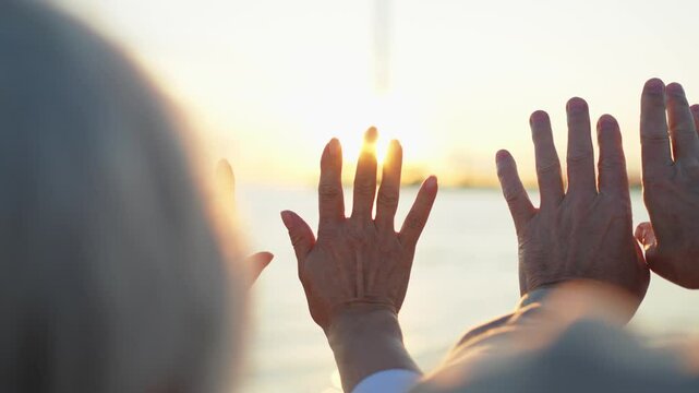 Senior couple hands at sunset. Old man woman pulls hand touching sun. Sunlight passing through fingers closeup shining sun. People stretching out hand to sun. Religion helping hand. Prayer in religion