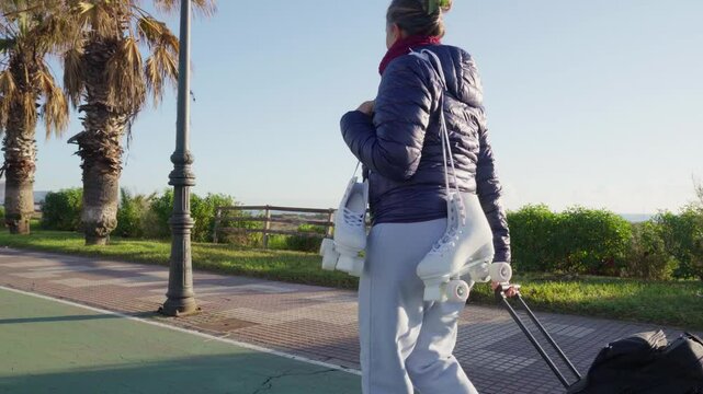 Active senior woman enjoys a healthy lifestyle, walking with rollerskates and a trolley bag along a seaside promenade