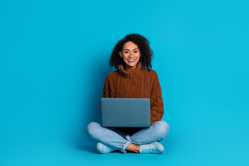 Naklejka premium Smiling young woman with laptop on blue background presenting casual and trendy lifestyle