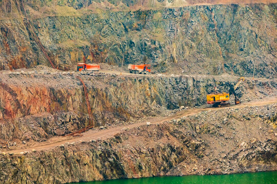 Mineral resources in Ukraine. Dump trucks and excavator on the slope of a large granite quarry and open-pit mining (strip mining)