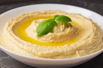 A plate of homemade hummus with olive oil on dark stone table close up. Arabic cuisine.