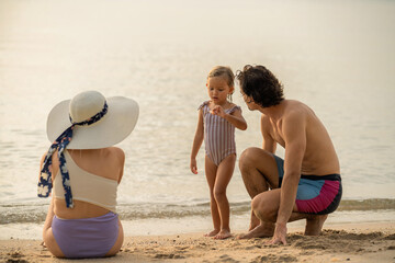 Family enjoys a beach day with child at sunset shore, creating lasting memories together in warm...