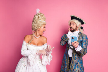 Historical theme party couple in vintage aristocratic costumes with pink backdrop showcasing elegance and humor