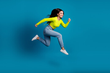 Fototapeta premium Energetic young woman in casual outfit happily leaping against a vibrant blue background