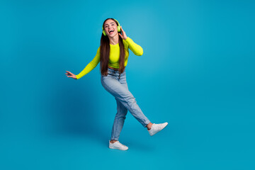 Happy young woman with headphones enjoying music on vibrant blue background in casual stylish outfit
