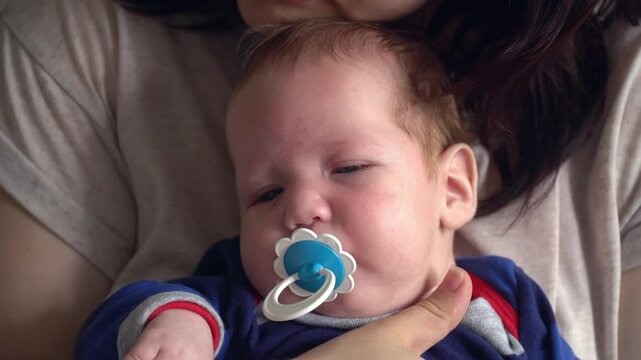 Close-up of a newborn baby sucking a pacifier and falling asleep. Mom holds the baby in her arms