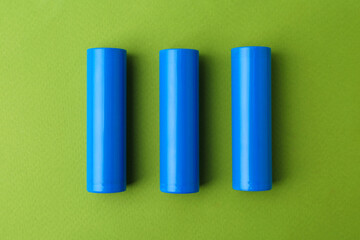 Fototapeta premium Three AA cell batteries on green background, top view