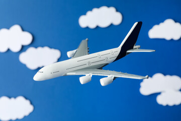 Plane model flying among paper clouds against blue background, closeup