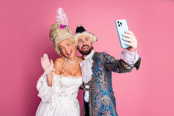 Couple in period costumes taking selfie against pink background at themed party