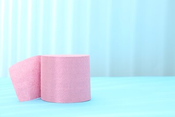 Pink toilet paper roll on light blue background, space for text