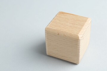 One wooden cube on light grey background, closeup. Space for text