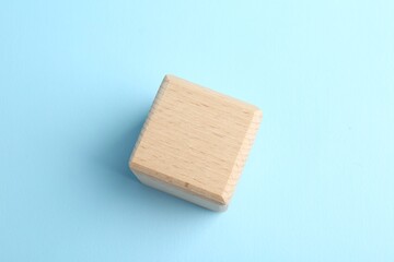 One wooden cube on light blue background, top view. Space for text