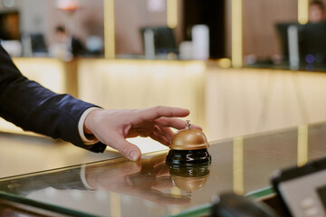 Medium close up of unrecognizable male hand ringing hotel service bell on reception desk
