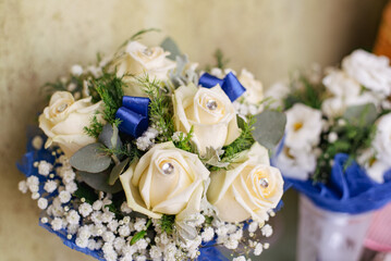 Elegant bridal bouquet featuring ivory roses, baby's breath, and greenery, accented with blue ribbons and sparkling gems. Perfect for wedding decorations, romantic occasions, and floral arrangements.