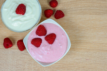 On a wooden table, there are two bowls filled with yogurt and fresh raspberries