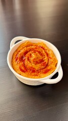 Delicious homemade hummus with baked carrot sprinkled paprika and za'atar in a white plate on a black background