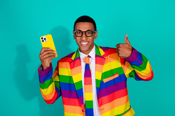 Colorful man in rainbow suit holding a phone giving a cheerful thumbs-up with a teal background