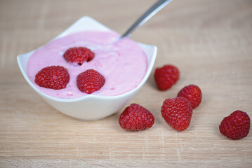 A bowl of yogurt topped with raspberries and a serving spoon