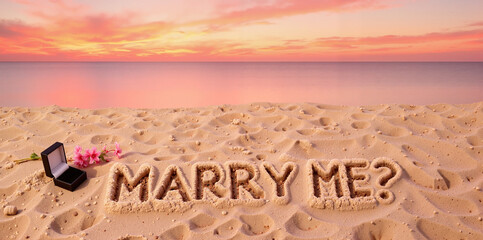 "MARRY ME?" proposal message written in sand at sunset beach - romantic engagement concept for wedding websites, relationship blogs, and love stories