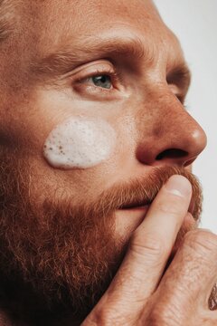 close up of a man applying a hydrating skincare product on his cheeck, masculine