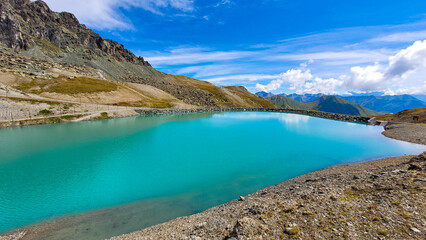 Panoramic view of the alpine lake with turquoise water, surrounded by mountain peaks, against the...