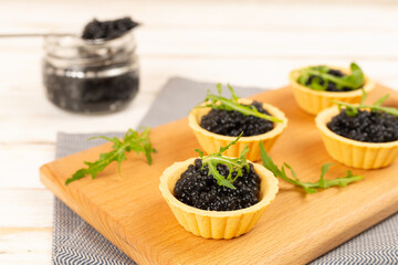 Tartlets with black caviar served on on wooden table