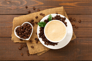Cup of coffee with coffee beans and leaves on wooden background,top view
