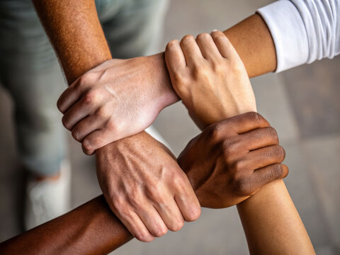 Four diverse hands clasped together in unity symbolizing strength and collaboration indoor close-up inspirational