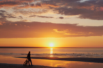Fototapeta premium Golden summer sunset on the Baltic Sea coast: silhouette, bicycle, observer, amazing clouds, Gulf of Finland.