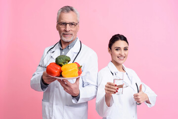 Portrait of smiling male and female doctors with stethoscopes holding water and plate of vegetables...
