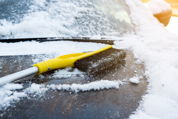 Winter scene of a car buried in snow, with a yellow brush clearing the windshield, in a sunny...
