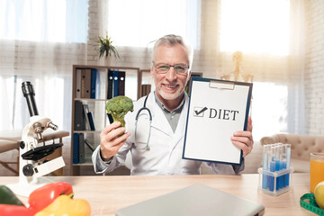Doctor sitting at desk in office with microscope and stethoscope. Man is holding diet sign.