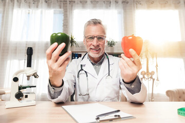 Doctor sitting at desk in office with microscope and stethoscope. Man is holding red and green...