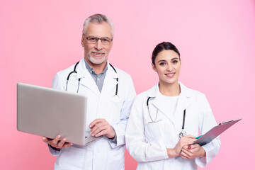 Portrait of smiling male and female doctors with stethoscopes holding laptop and clipboard isolated.