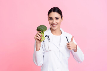 Portrait of smiling female doctor with stethoscope holding broccoli isolated.