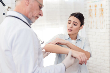 Doctor with stethoscope and female patient in office. Doctor is examining woman's arm.
